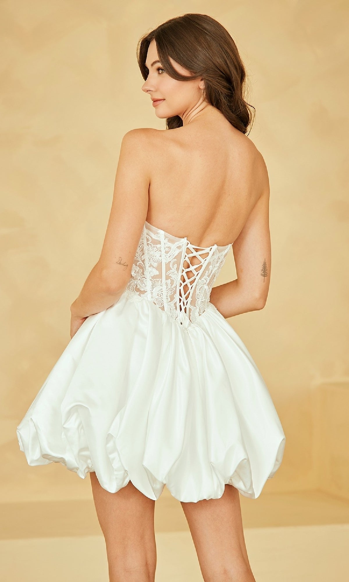 Woman showing the back of a short white bubble-hem dress she's wearing in front of a beige background.